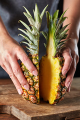 Wall Mural - Two halves of ripe organic pineapple hold the girl's hands on an old wooden board. Exotic fruit