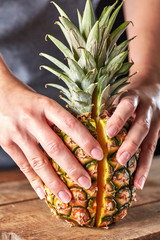 Wall Mural - Fresh halves of an exotic pineapple hold the girl's hands on a wooden kitchen board. Vitamin fruit