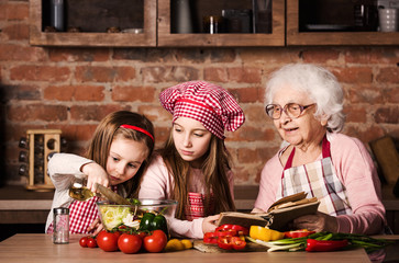 Two little sisters with granny cooking healthy vegetable salad together at kitchen at home