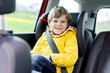 © Irina Schmidt - Adorable cute preschool kid boy sitting in car in yellow rain coat. Little school child in safety car seat with belt enjoying trip and jorney. Safe travel with kids and traffic laws concept