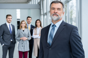 Businessteam in office, Happy Senior Businessman in His Office is standing in front of their team.