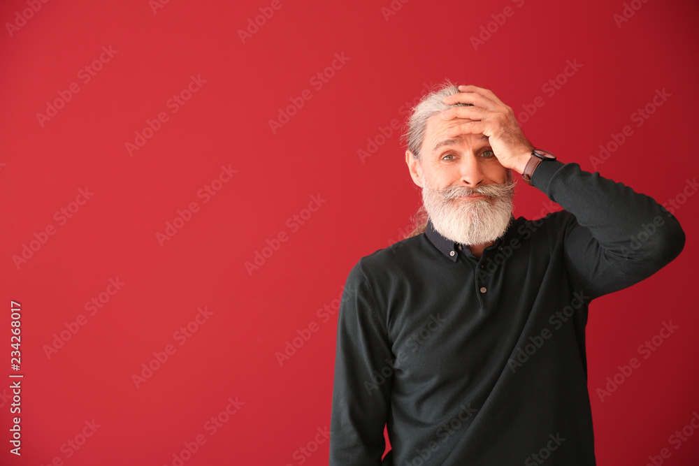 Emotional senior man after making mistake on color background