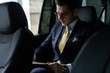 © opolja - Young businessman sitting on back seat of the car, while his chauffeur is driving automobile.
