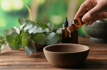 Woman pouring eucalyptus essential oil into bowl on wooden table