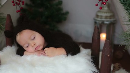 Canvas Print - Cute toddler baby boy in handmade knitted bear costume, sleeping in wooden bed in teepee, decorated for Christmas