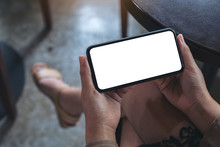 Mockup Image Of Woman's Hands Holding Black Mobile Phone With Blank White Screen Horizontally For Watching While Sitting In Cafe