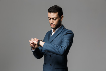 Image of serious arabic businessman 30s in formal suit looking at wristwatch, isolated over gray background