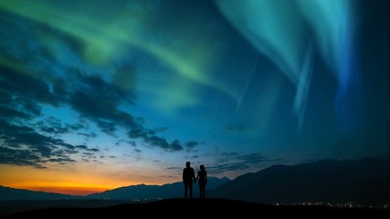 Wall Mural - The man and a woman standing on a mountain against a northern light. time lapse