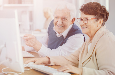 Poster - Senior man pointing finger at computer screen and explaining problem to his classmate during computer classes at third age university