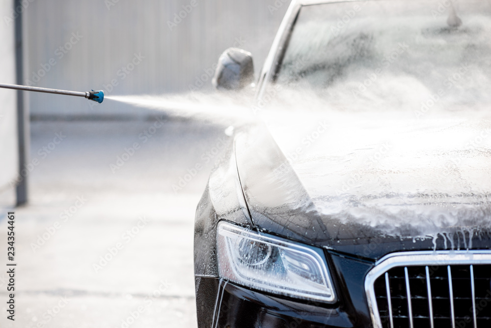 Close-up of a car under the water jet during the washing process on a self service car wash - obrazy, fototapety, plakaty 