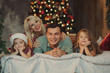 Merry Christmas and Happy Holidays! Cheerful parents and  and two little children having fun and playing together near Christmas tree on the bed in living room