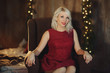 Portrait of a young blond woman, sitting on soft chair in dark room. Christmas and holiday concept