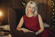 Portrait of a young blond woman, sitting on soft chair in dark room. Christmas and holiday concept