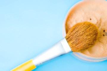 Beauty box, crumbly matte mineral powder with a special brown beautiful wooden brush from natural nap for makeup on a warm blue background. Flat lay. Top view