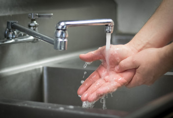 Handwashing hands; washing with soap and water at stainless steel sink.