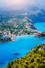 Wall Mural - Assos village in morning light, Kefalonia. Greece. White lonely yacht in beautiful turquoise colored bay lagoon water surrounded by pine and cypress trees along the coastline