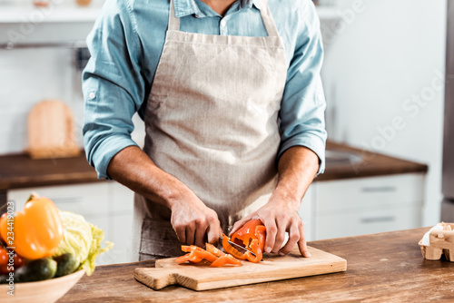 Cuadros en Lienzo mid section of young man in apron cutting fresh pepper in kitchen