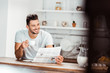 © LIGHTFIELD STUDIOS - selective focus of smiling young man holding cup of coffee and reading newspaper in kitchen at morning