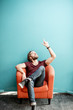 © rh2010 - Portrait of a young caucasian bearded man with long hair showing with hands on the colorful background sitting on the chair. Image with copy space