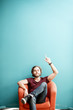© rh2010 - Portrait of a young caucasian bearded man with long hair showing with hands on the colorful background sitting on the chair. Image with copy space