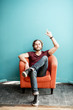 © rh2010 - Portrait of a young caucasian bearded man with long hair showing with hands on the colorful background sitting on the chair. Image with copy space