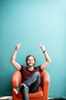 © rh2010 - Portrait of a young caucasian bearded man with long hair showing with hands on the colorful background sitting on the chair. Image with copy space