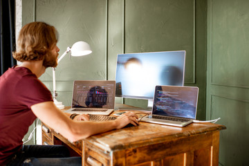 Wall Mural - young programmer writing a program code sitting at the workplace with three monitors in the office o