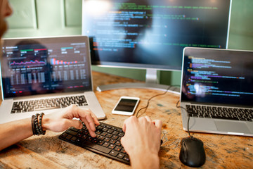 Wall Mural - young programmer writing a program code sitting at the workplace with three monitors in the office