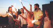 © NDABCREATIVITY - Friends enjoying a rooftop party and dancing with sparklers