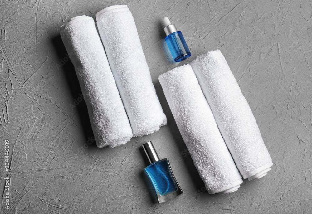 Rolled clean soft towels with cosmetics on grey background
