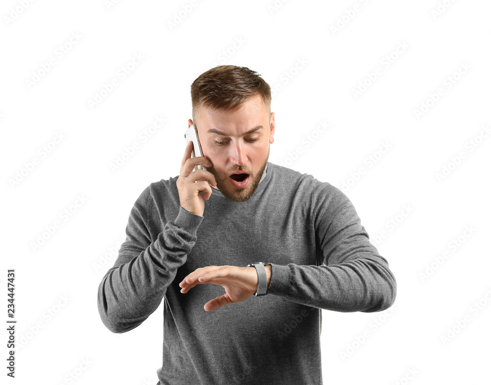 Emotional man looking at his watch while talking by phone on white background