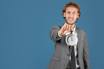 Stressed businessman with alarm clock on blue background