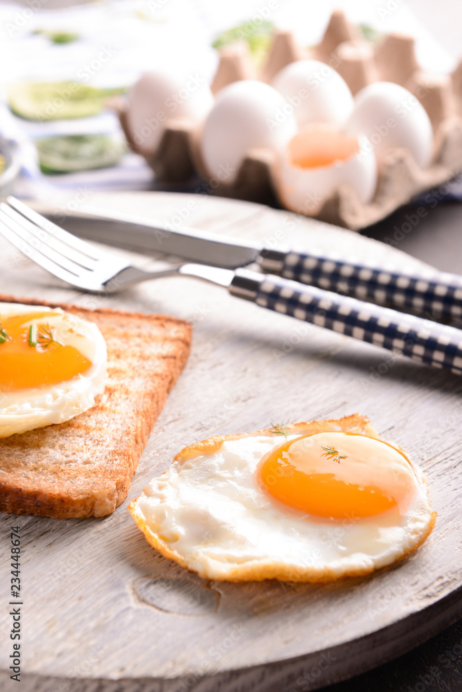 Toasted bread with tasty fried eggs on wooden board