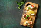 Fototapeta Mapy - Italian Antipasti snacks set for Wine. Variety Brushetta with Soft Cheese, Pear, Radish, Salmon and Dried Tomatoes served on a rustic wooden board on a stone table. Top view. Copy space.