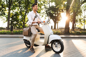 Poster - Young business man walking outdoors on scooter.