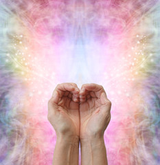 Wall Mural - Healers hands making a humble heart shape - female hands in open cupped position creating a heart shape on a rainbow coloured sparkling energy formation background  with copy space above
