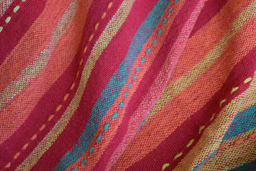  Bright red-pink fabric with orange, khaki and pale yellow stripes arranged in folds. Top view background texture. Close up. Copy space.