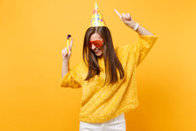 Joyful Woman In Orange Funny Glasses Birthday Party Hat With Playing Pipe Rising Hands Pointing Index Fingers Up, Dancing Celebrating Isolated On Yellow Background. People Sincere Emotions, Lifestyle.