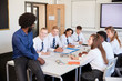 © Monkey Business - Male High School Teacher Sitting At Table With Teenage Pupils Wearing Uniform Teaching Lesson