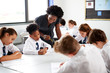 © Monkey Business - Female High School Tutor Helping Students Wearing Uniform Seated Around Tables In Lesson