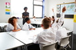 © Monkey Business - High School Students Wearing Uniform Raising Hands To Answer Question Set By Teacher In Classroom