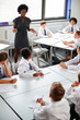 © Monkey Business - Female High School Tutor Helping Students Wearing Uniform Seated Around Tables In Lesson