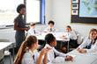 © Monkey Business - Female High School Tutor Helping Students Wearing Uniform Seated Around Tables In Lesson