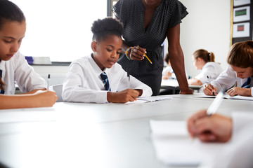 Wall Mural - Female High School Tutor Helping Students Wearing Uniform Seated Around Tables In Lesson