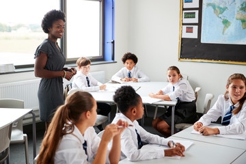 Wall Mural - Female High School Tutor Helping Students Wearing Uniform Seated Around Tables In Lesson