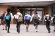 © Monkey Business - Group Of High School Students Wearing Uniform Running Into School Building At Beginning Of Class