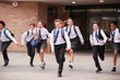 © Monkey Business - Group Of High School Students Wearing Uniform Running Out Of School Buildings Towards Camera At The End Of Class