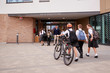 © Monkey Business - Group Of High School Students Wearing Uniform Arriving At School Walking Or Riding Bikes Being Greeted By Teacher