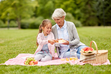 Canvas Print - family, leisure and people concept - happy grandmother and granddaughter having picnic at summer park