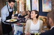 Waiter with dishes serving man and woman friendly company indoors